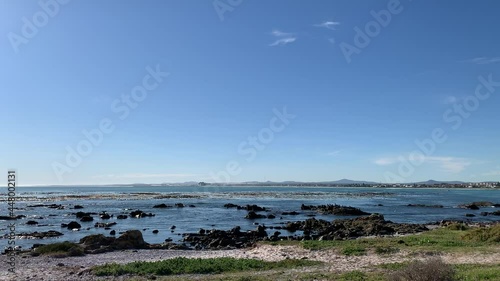 Rocky beach waves crashing over rocks seaweed in the sea water with sun glimmering Melkbosstrand beach photo