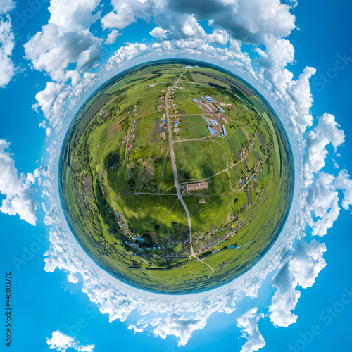 rural landscape - streets, houses with large courtyards among the plain and green fields under a blue sky with large white clouds and dark shadows from them on the ground - aerial small planet view