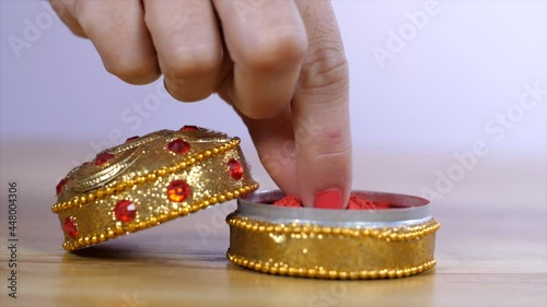 Female hands taking a bit of vermilion / Sindoor to celebrate an auspicious occasion . Closeup shot of a beautiful golden Sindoor box decorated with beads kept on a wooden table - Hindu marriage an... photo