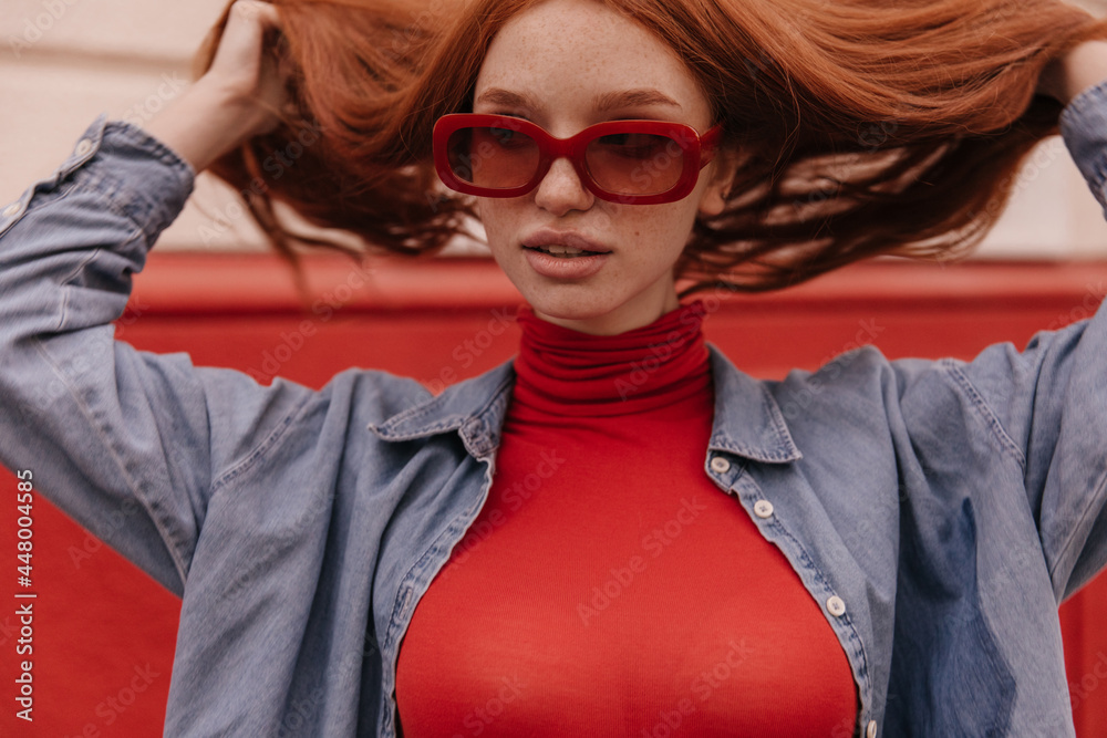 Beauty portrait of young stylish girl posing outdoors. Adorable ginger with  long smooth hairstyle, freckles, trendy sunglasses, red turtleneck and blue  shirt, looking aside Stock Photo | Adobe Stock