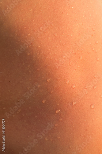 Water drops on human skin in the sunlight. Abstract background, skin texture. Close up, vertical
