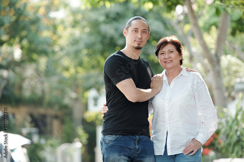 Portrait of Asian mature woman smiling at camera while standing outdoors together with her elder son © DragonImages