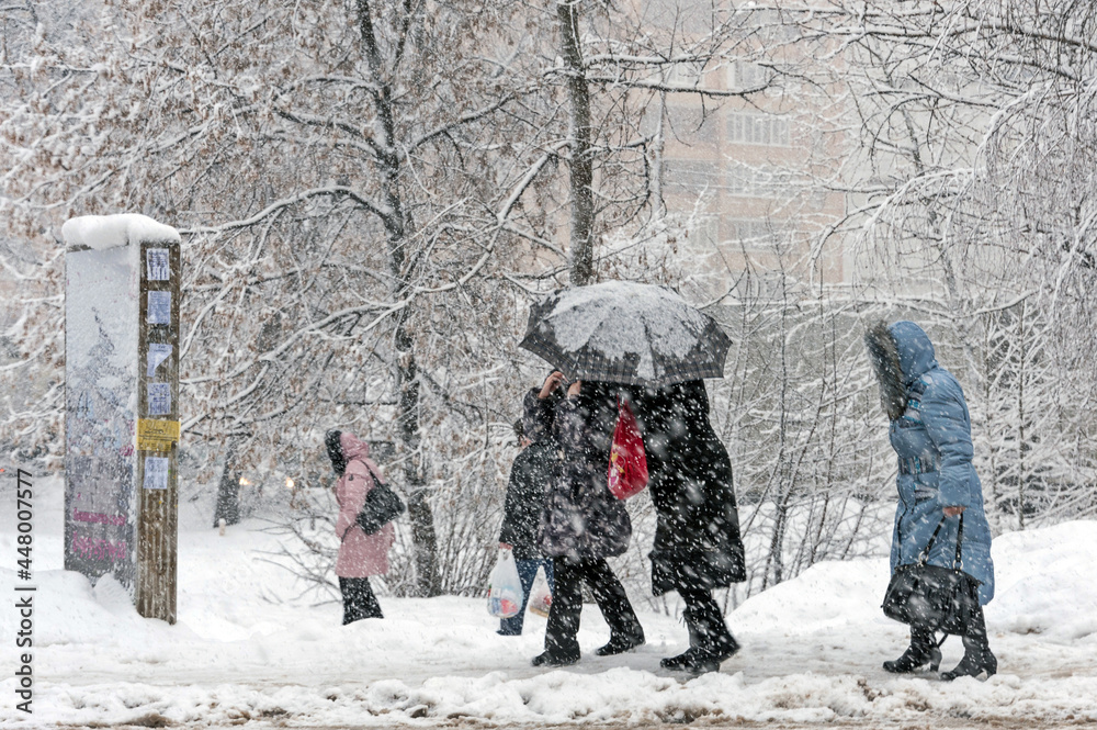 It is snowing heavily in the city. People hide from the snow under an umbrella