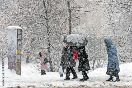 Fototapeta Naklejka Na Ścianę i Meble -  It is snowing heavily in the city. People hide from the snow under an umbrella