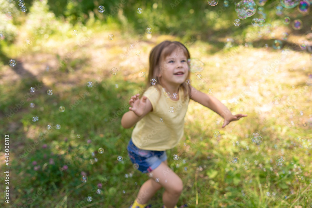 cute baby girl catches a lot of soap bubbles on a summer day, focus on bubbles, child in blur cute baby girl catches a lot of soap bubbles on a summer day, focus on bubbles, child in blur