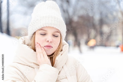 teen girl has a toothache outdoor in winter. tooth enamel reacts to cold