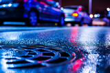 Rainy night in the parking shopping mall, rows of parked cars. Close up view of a hatch at the level of the asphalt