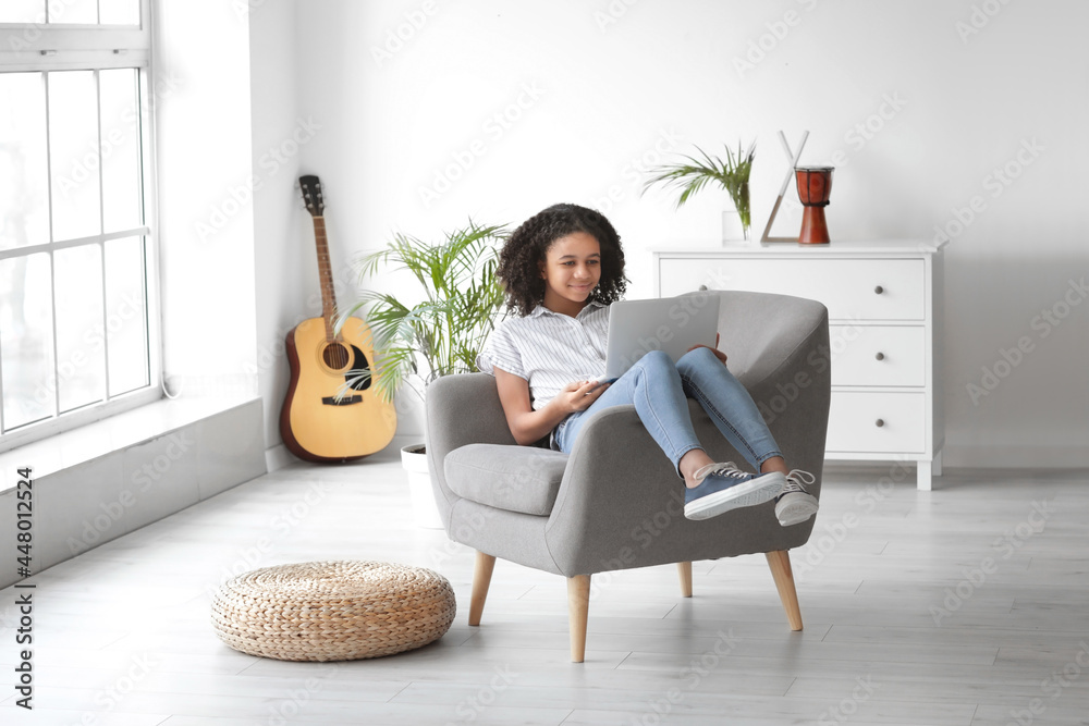 African-American girl with laptop sitting in armchair at home African-American girl with laptop sitting in armchair at home
