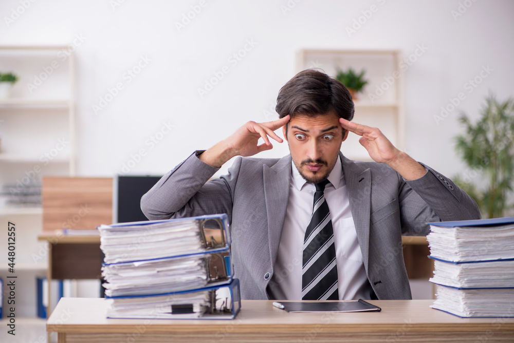Young male employee unhappy with excessive work in the office Young male employee unhappy with excessive work in the office