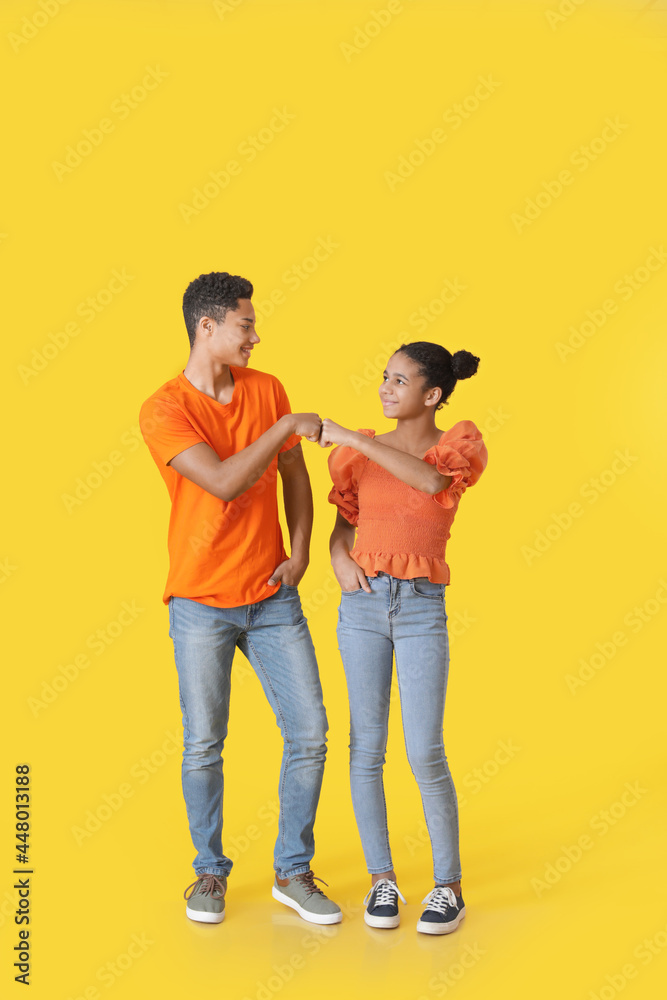 Obraz premium African-American brother and sister bumping fists on color background