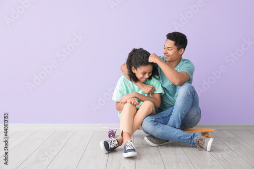 African-American brother and sister with skateboards sitting near color wall
