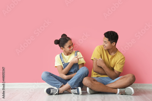 Valokuva African-American brother and sister sitting near color wall