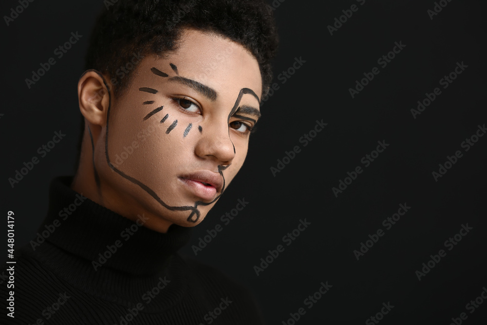 Young African-American guy with paint on face against dark background