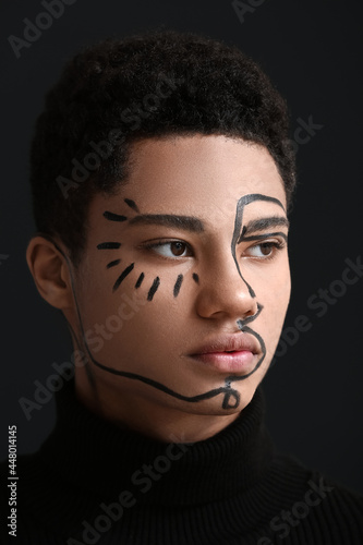 Young African-American guy with paint on face against dark background