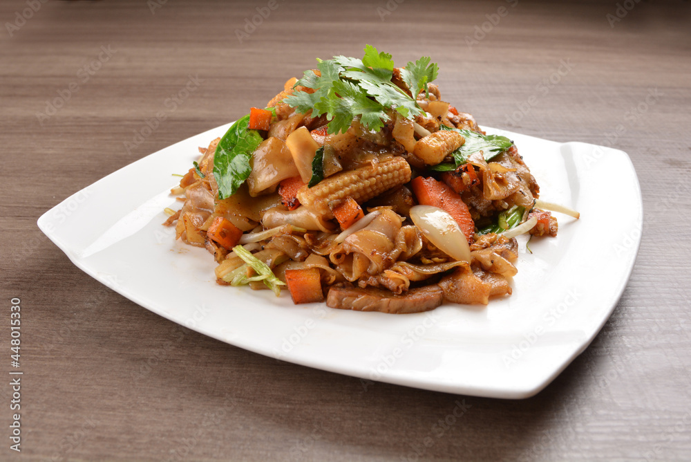 wok stir fried kway teow rice noodle mee goreng with vegetable in spicy soy chilli sauce on wood background asian halal vegan menu wok stir fried kway teow rice noodle mee goreng with vegetable in spicy soy chilli sauce on wood background asian halal vegan menu