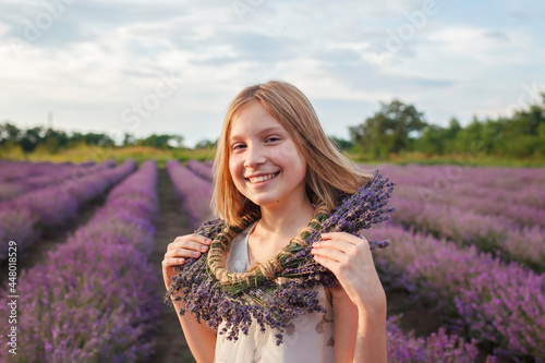 Teenage girl enjoys the scenery of lavender field. Dreamy teenager with floral wreath walking among purple flowers. Calm landscape, escape to beauty of nature, summer lifestyle