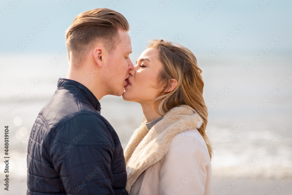 Young couple kissing outdoor.Stunning outdoors portrait of young stylish fashion couple posing in spring sea background. Young couple kissing outdoor.Stunning outdoors portrait of young stylish fashion couple posing in spring sea background.