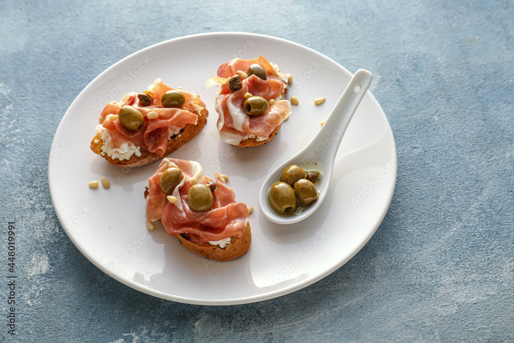 Tasty bruschettas with cheese, prosciutto and olives on color background