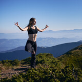 Slim woman in sportswear meditating on fresh air on beautiful blue sky background. Concept of harmony with nature.