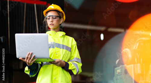 Female Quality control inspector checking workers at factory. Woman engineer with yellow hard hat helmet working on laptop computer inside industrial manufacturing factory photo