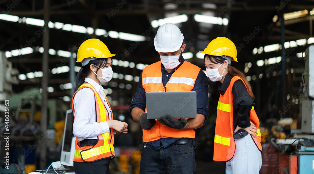 Engineers people are brainstorming solving problems of heavy industrial machinery. Worker man and asian woman wearing face mask prevent covid-19 virus and protective hard hat. . Engineers people are brainstorming solving problems of heavy industrial machinery. Worker man and asian woman wearing face mask prevent covid-19 virus and protective hard hat. .