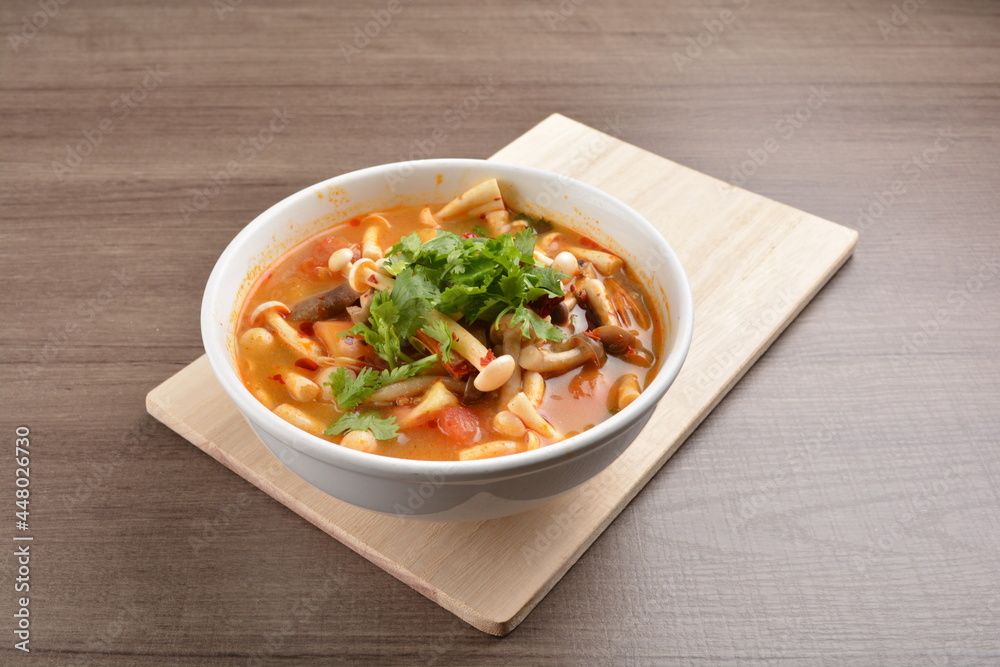 cook hot and spicy tom yum soup with mushroom and mixed vegetables in white bowl on wood background asian halal vegan menu cook hot and spicy tom yum soup with mushroom and mixed vegetables in white bowl on wood background asian halal vegan menu