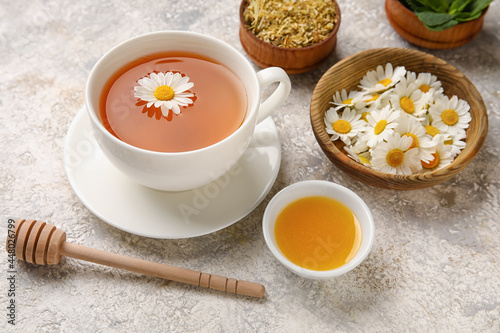 Composition with cup of chamomile tea, flowers and honey on light background