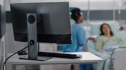 Tableau sur toile Hospitalized woman resting in bed while asisstant with black skin monitoring sickness symptom writing medical expertise on clipboard