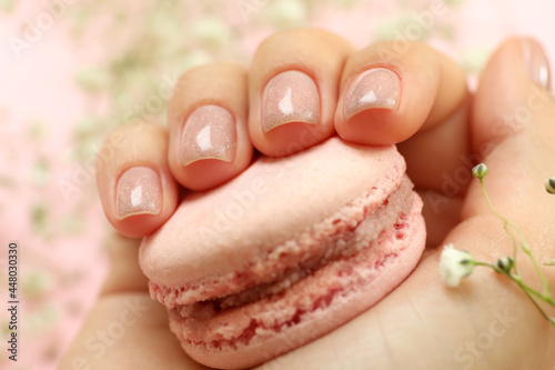 Female hand with glitter manicure holds macaroon, close up