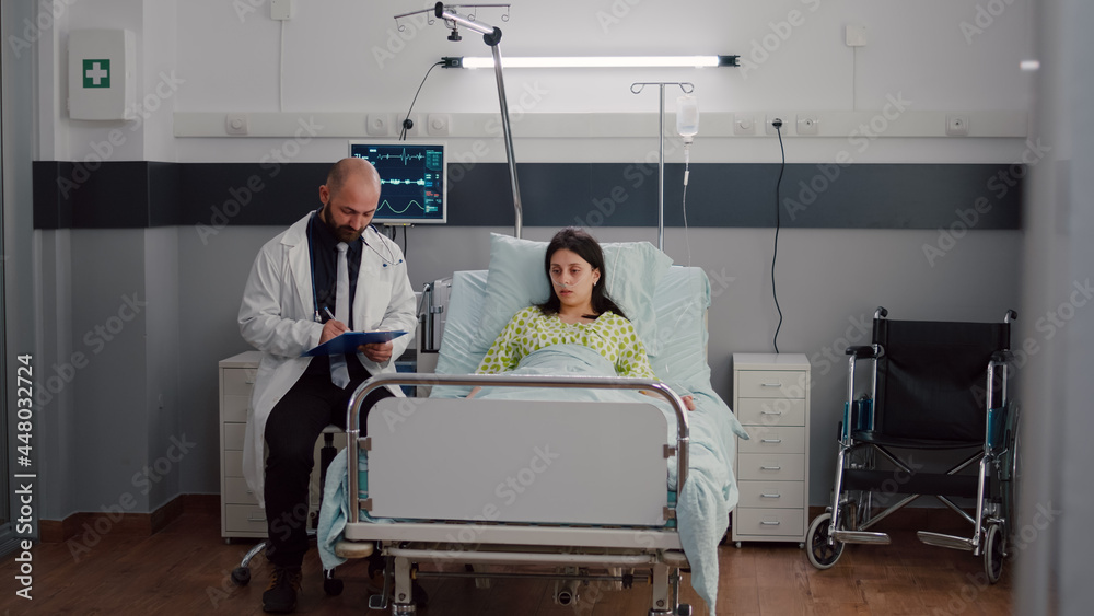 Front view of sick woman resting in bed discussing with oncologist man doctor about test results. Practitioner writing sickness treatment on clipboard monitoring healdcare recovery in hospital ward Front view of sick woman resting in bed discussing with oncologist man doctor about test results. Practitioner writing sickness treatment on clipboard monitoring healdcare recovery in hospital ward
