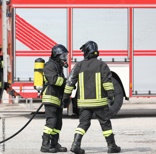 two firefighters in uniform with oxygen cylinder during emergency and fire truck in the background