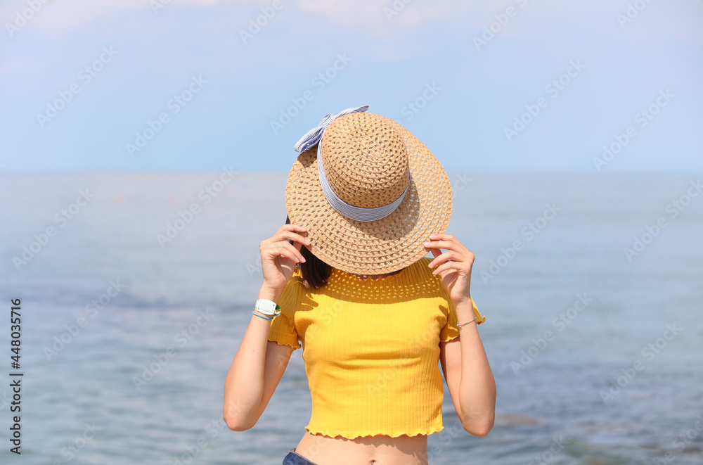 girl in yellow shirt covers her face with a wide straw hat