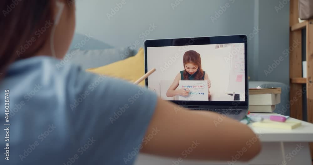 Young Asia girl with casual use computer laptop video call learn online with teacher write lecture notebook living room at house. Isolate education online e-learning coronavirus pandemic concept. Young Asia girl with casual use computer laptop video call learn online with teacher write lecture notebook living room at house. Isolate education online e-learning coronavirus pandemic concept.