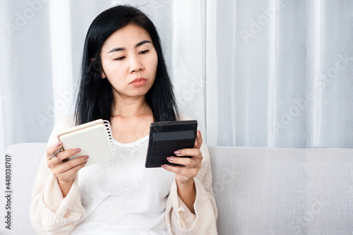 sad Asian woman holding calculator with list of debt, expenses on notepad , female having financial problem during quarantine