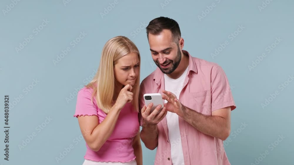 Young couple two friends family man woman in pink clothes together hold in hand use mobile cell phone point on it say wow search isolated on pastel plain light blue color background studio portrait Young couple two friends family man woman in pink clothes together hold in hand use mobile cell phone point on it say wow search isolated on pastel plain light blue color background studio portrait