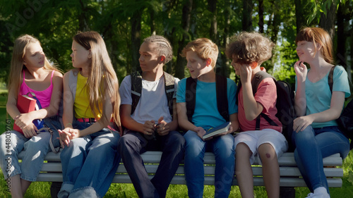 Group of friendly multiethnic kids sitting on bench in park