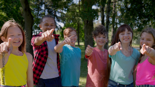 Medium shot of multiethnic kids point finger at camera and laugh outdoors