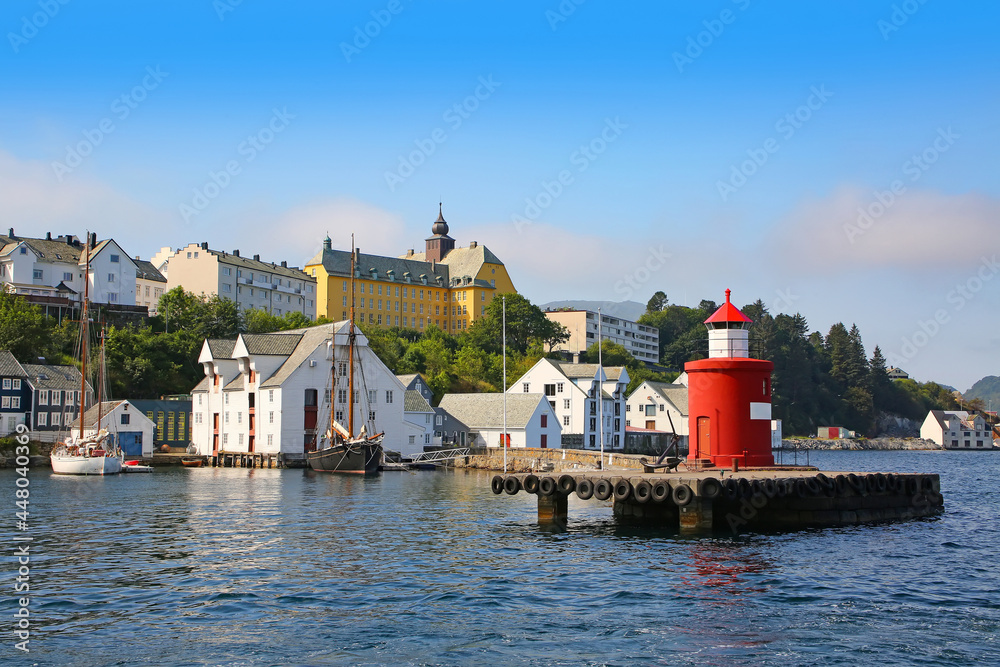 Historic buildings, pier and traditional fishing boats along the waterfront of the harbour. Lighthouse in the foreground of the getty, Alesund, Norway.