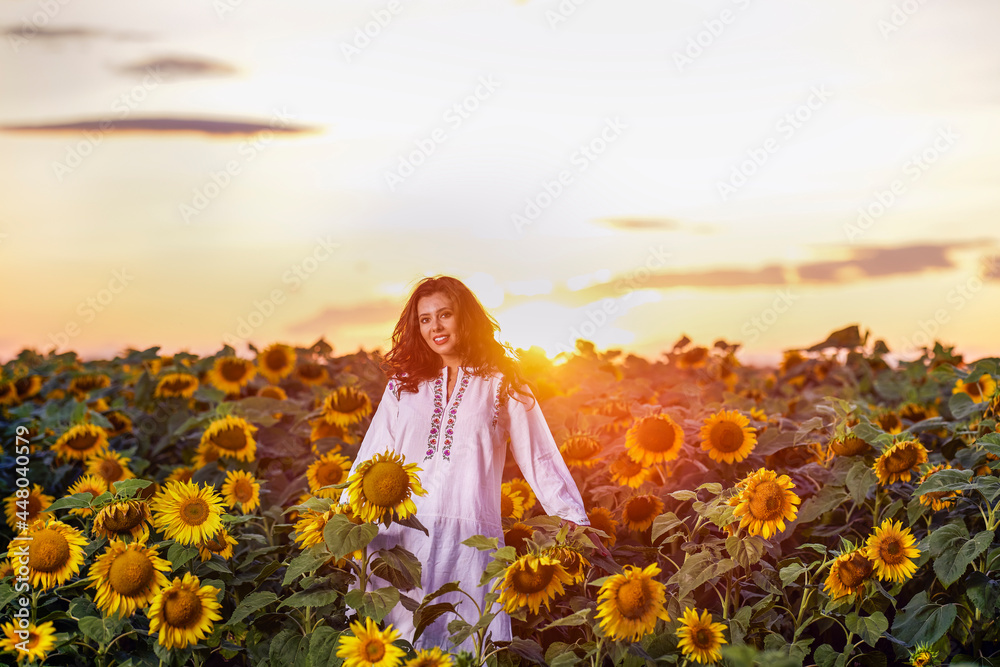 Beautiful woman enjoying nature in the sunflower field at sunset. Traditional clothes. Attractive brunette woman with long and healthy hair. Beautiful woman enjoying nature in the sunflower field at sunset. Traditional clothes. Attractive brunette woman with long and healthy hair.