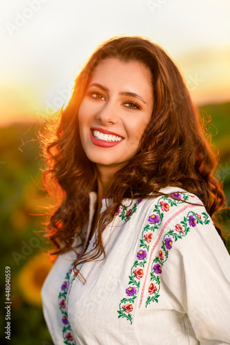 Beautiful woman enjoying nature in the sunflower field at sunset. Traditional clothes. Attractive brunette woman with long and healthy hair.