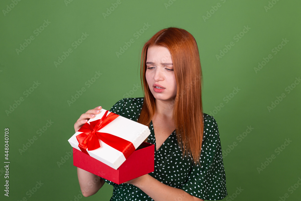 Young red hair woman on green background with gift box unhappy sad disappointed Young red hair woman on green background with gift box unhappy sad disappointed