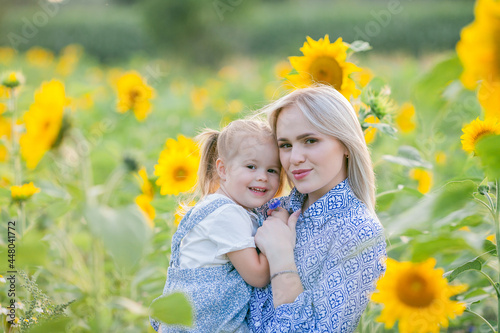 Mom with a little daughter 3 years old in a sunflower field. Summer sunset. Family. Happiness.