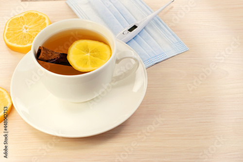Lemon tea in a white cup on a wooden table near a medical mask and a thermometer. Medical concept. Self-medication