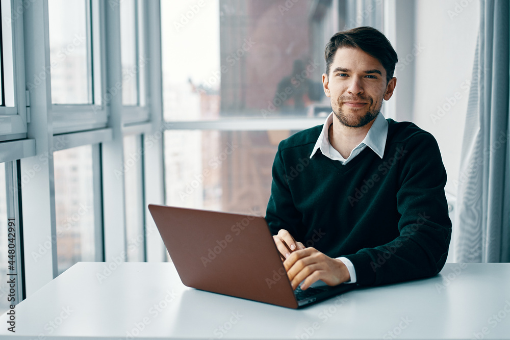 A man sits at a table in front of a laptop working via the Internet A man sits at a table in front of a laptop working via the Internet