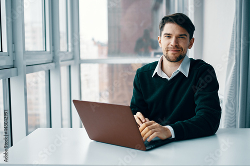 A man sits at a table in front of a laptop working via the Internet