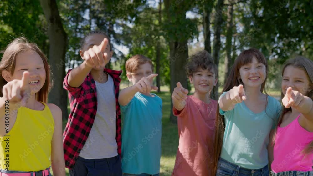 Medium shot of multiethnic kids point finger at camera and laugh outdoors