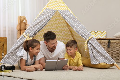 Father with children reading book in wigwam at home