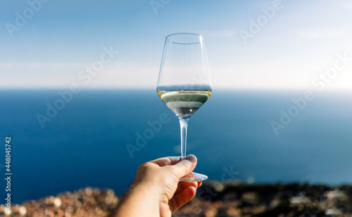 Hand holding glass of white wine with sky sea and beach on background - Travel vacation concept