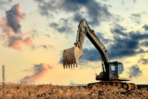 Excavator on earthworks at construction site on sunset background. Heavy machinery and equipment for earthmoving photo