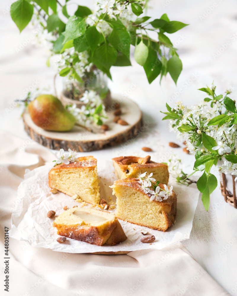 Pear cake. Summer dessert with fruit on a white table. A piece of cake on a ceramic plate. Fresh homemade cakes. Summer still life with cherry blossom